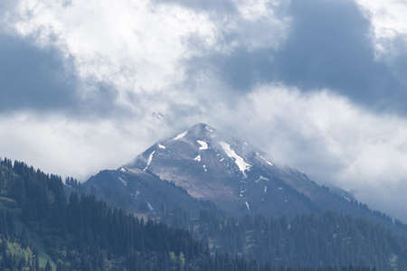 Mountain peak in the form of a triangle in cloudy weather. Coniferous forests on the slopesの写真素材