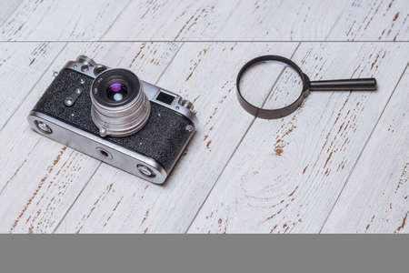 Old retro camera and magnifying glass on white boards. vintage photo