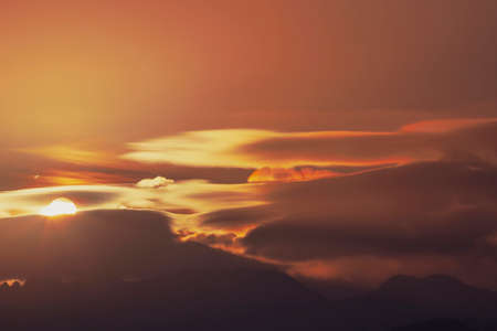 The sun rises among the clouds above the silhouettes of mountain hills. Morning haze.の写真素材