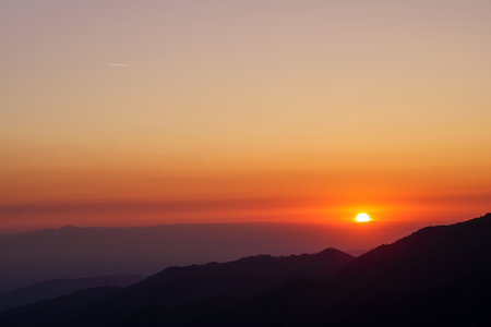 The sun rises over the silhouette of a mountain range. blue hourの写真素材
