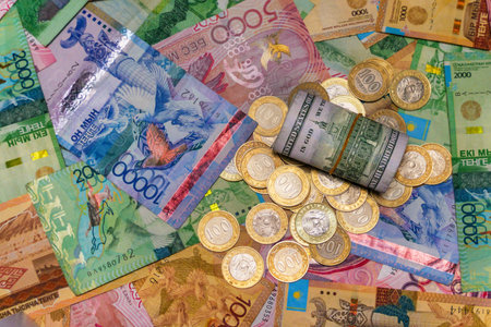 A folded $100 bill lies on top of coins and tenge bills. Currency exchangeの写真素材