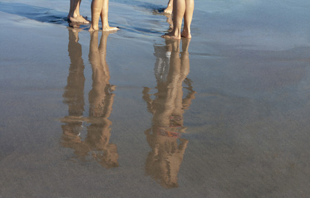 people at the beach shore with reflection on wet sand
