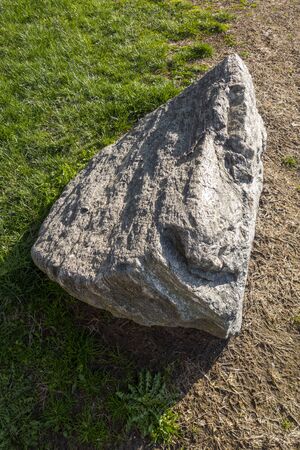 large stone sitting on soil and grass lawn