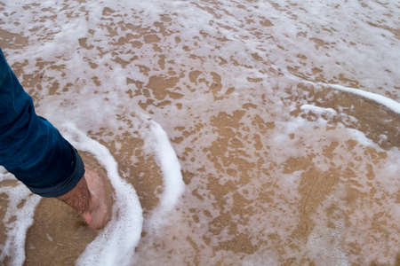 jeans and feet in wet beach sandの写真素材