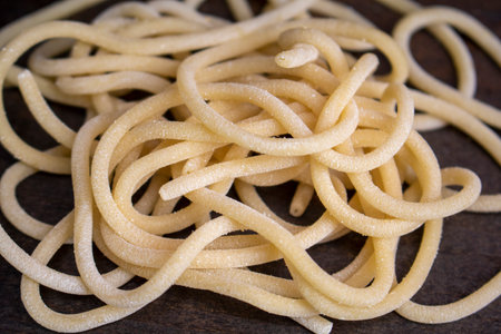 perciatelli, fresh made pasta on a dark wood surface