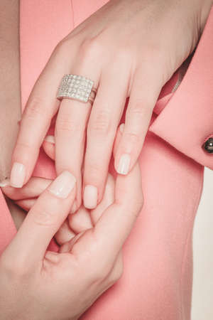 Beautiful hands of a woman wearing a diamonds ring on a pink jacketの写真素材