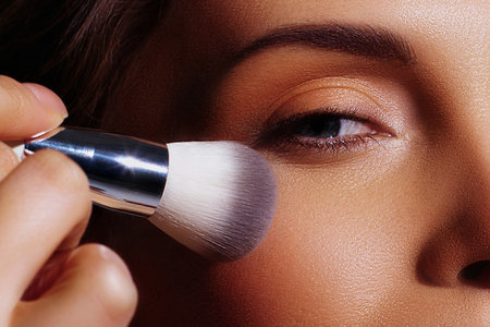 Applying makeup with a brush on cheekbone of beautiful white woman. Close-up of makeup artist's workの写真素材
