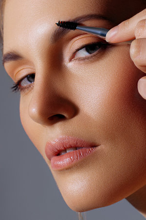 Eyebrow brushing on white adult model in close-up. Radiant skin, natural shades and neatness in makeupの写真素材