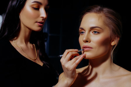 Makeup artist paint lips of model. Makeup in natural shades, backstage workの写真素材