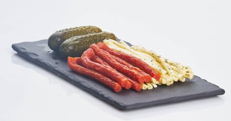 cheese and sausages and cucumbers on black plateの写真素材