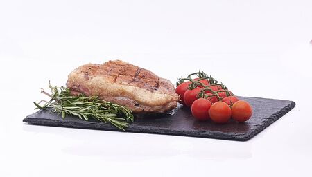 pork chop, cherry tomatoes and cheese on black plate on whiteの写真素材