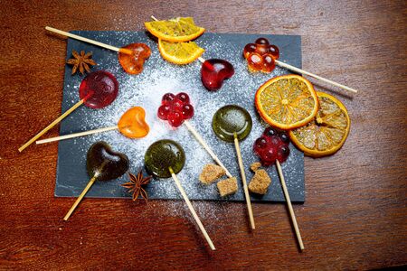 multi-colored candies on a black plate with candied fruits on woodの写真素材