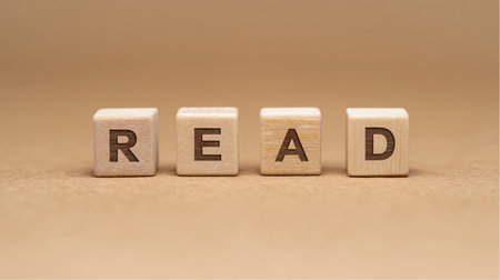 Four small, wooden blocks display the letters R, E, A, and D respectively, spelling the word read. They are set against a plain tan background, promoting literacy and knowledge.の素材