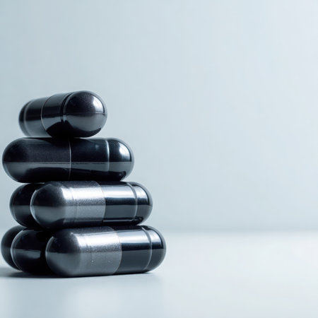 Several black capsules are stacked vertically, forming a small tower on a light gray surface. The background is a smooth, gradient gray. The capsules appear smooth and glossy.の素材
