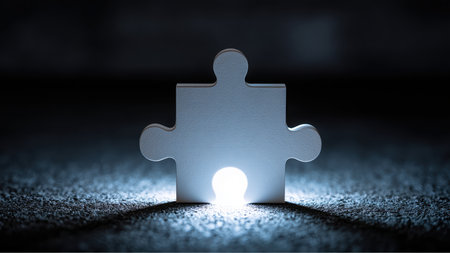 A single white jigsaw puzzle piece stands vertically on a dark, textured surface. A bright light shines from behind the piece, illuminating the ground in front of it.の素材