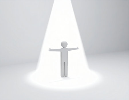 A simple, white, three-dimensional figure with outstretched arms stands beneath a concentrated beam of light on an otherwise plain white surface. The intense illumination highlights the solitary individual.の素材