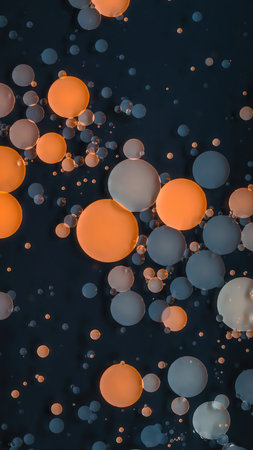 A visually striking abstract composition featuring a multitude of spherical objects, resembling bubbles or beads, floating within a dark liquid medium. The spheres vary in size, predominantly showcasing vibrant orange and muted blue hues, with some appearing in lighter shades. They are scattered randomly across the frame, creating a dynamic and textured surface. The arrangement suggests subtle movement and fluidity, making it suitable for scientific, artistic, or decorative contexts.の素材