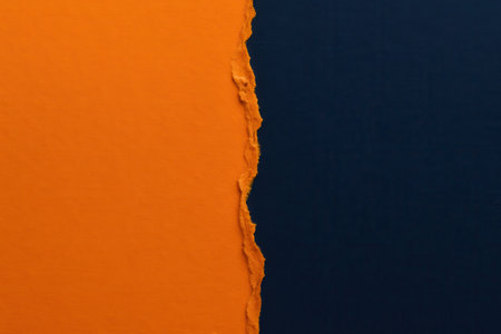 A close-up view of a vibrant orange surface meeting a deep, dark blue background, separated by a distinct, rough torn edge. The textured tear creates a dramatic division between the two contrasting hues, evoking a sense of artistic disruption and visual tension. This abstract composition highlights the tactile quality of the ripped material and the bold interplay of color, making it suitable for various creative design projects requiring dynamic backgrounds or graphic elements. The stark separation emphasizes division, transition, or juxtaposition, offering a compelling visual element.の素材