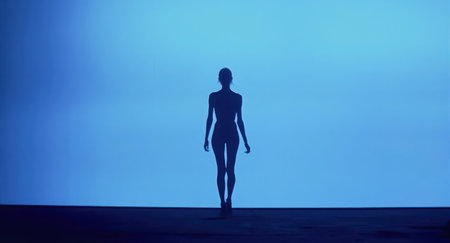 A dark, silhouetted figure stands against a vibrant blue gradient background, creating a minimalist and futuristic scene. This conceptual representation suggests themes of technology, AI, virtual reality, solitude, and the digital future.の素材