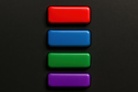 A close-up view of four brightly colored rectangular objects stacked vertically against a dark, solid background. The top object is red, followed by blue, then green, and finally purple at the bottom. Each shape has smooth, rounded edges and a glossy finish, reflecting a subtle light source. The arrangement creates a distinct pattern of vibrant hues.の素材