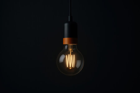 A single incandescent light bulb is illuminated, showcasing its intricate filament. The vintage-style bulb features a warm, amber glow, creating a striking contrast against the deep, dark background. It is suspended by a dark cable with a contrasting black and copper fixture. This minimalist composition emphasizes the bright light source, evoking themes of inspiration, creativity, innovation, and electric power. The scene represents a concept of a new idea or a solution coming to light.の素材