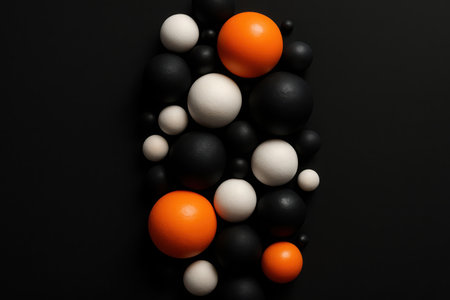 A top-down view presenting a dense cluster of spherical objects against a plain dark surface. The spheres vary in size and are colored black, white, and bright orange, creating a striking visual texture and an an abstract pattern. This arrangement offers a modern and dynamic background element.の素材
