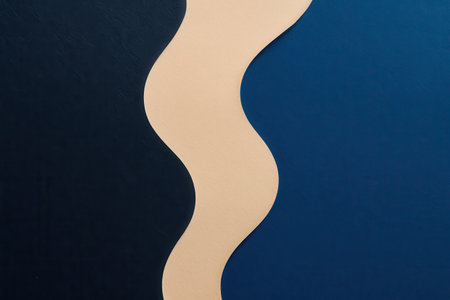 An abstract composition featuring a central, vertical, undulating beige element serving as a visual divider. To the left, the surface is a deep, dark blue, contrasting with the lighter, rich blue on the right. The overall presentation is clean, modern, and minimalist, ideal for backgrounds or graphic design elements.の素材