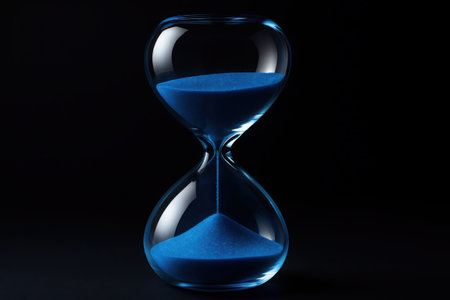 A crystal hourglass with vibrant blue sand steadily flowing from the upper chamber to the lower, set against a deep, dark background. It visually represents the passage of time, deadlines, and measurement.の素材