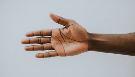 Detailed view of a persons open hand, showcasing the palm. The hand has a dark brown complexion and is positioned against a solid, light-colored backdrop. It conveys a sense of invitation or openness.の素材