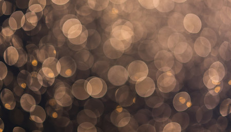 A panoramic visual of numerous warm golden bokeh lights against a dark, blurred backdrop, creating an abstract and luminous effect. The out-of-focus circular light sources give a sparkling, shimmering ambiance, ideal for celebrations, events, or decorative design elements. The overall impression conveys gentle light and depth, suitable for various creative projects.の素材