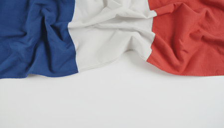 A flat lay shot of a crumpled French flag, featuring its iconic blue, white, and red vertical stripes. The textile flag rests on a clean white background, with significant blank space beneath, ideal for text or graphic overlays. It symbolizes France, patriotism, and European heritage.の素材