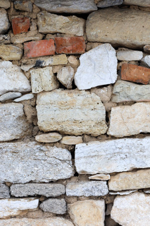Rough stones of different colors and sizes form a sturdy wall, showcasing a combination of white,...