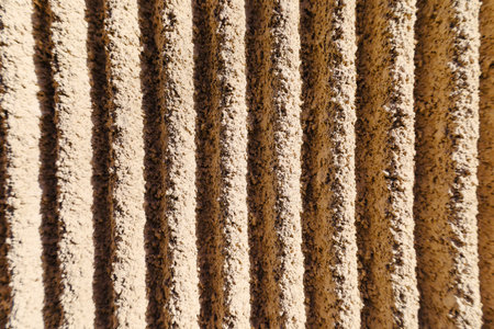 Vertical lines create a stunning visual rhythm on the surface of a sun kissed wall. The warm colors and textures draw the eye, evoking a sense of depth and warmth in a peaceful setting.の写真素材