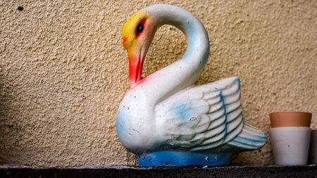 A charming ceramic swan in bright hues of white and yellow catches the light as it rests atop a weathered surface. Its cheerful presence adds a touch of whimsy to the surrounding space.の写真素材