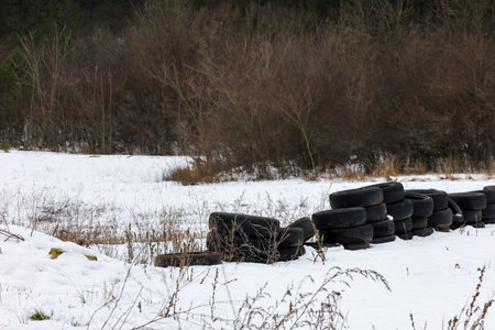 In a winter wonderland, a stack of worn black tires rests against a backdrop of white snow and...