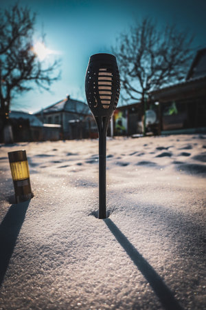 A solar lantern brightens a snowy yard, casting a warm glow against the cold. The sun shines...