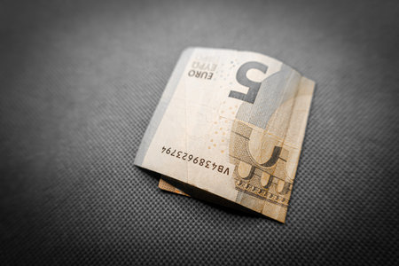 A five euro note rests softly on a bright green textile backdrop, showcasing intricate designs and...