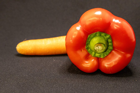 A vibrant red bell pepper and a fresh orange carrot are displayed on a dark surface, ready for healthy cooking.の写真素材