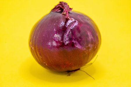 A single, vibrant red onion is prominently displayed on a bright yellow background, ready to add flavor to any dish.の写真素材