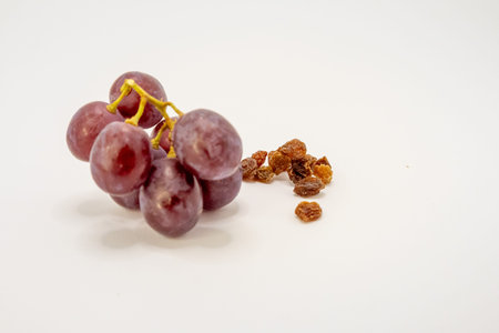 A bunch of red grapes and a pile of raisins on white, illustrating the fresh and dried forms of the fruit.の写真素材