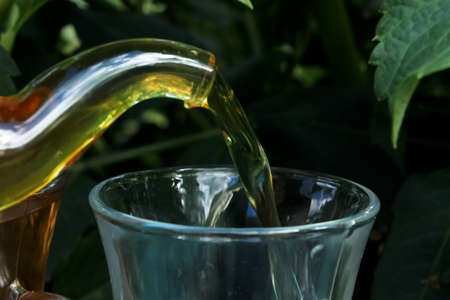 Tea is poured from a glass teapot into a glass cup in the gardenの写真素材