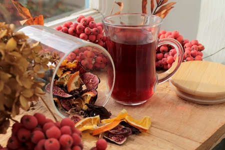 Tea with dried figs, pomegranate leaves and orange slices in a jar and in a glass on a wooden windowsillの写真素材