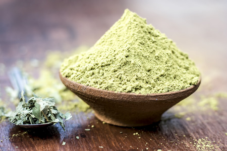 Raw organic powder of Henna,Lawsonia inermis in a clay bowl with its dry leaves on wooden surface.の写真素材
