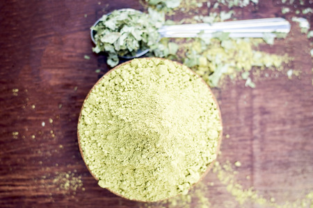 Raw organic powder of Henna,Lawsonia inermis in a clay bowl with its dry leaves on wooden surface.