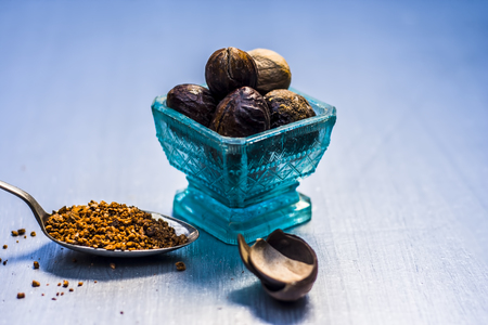 Close up of Nutmeg,Jaiphal,Myristica fragrans in a glass container with its powder on wooden surface.の写真素材