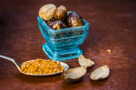Close up of Nutmeg,Jaiphal,Myristica fragrans in a glass container with its powder on wooden...