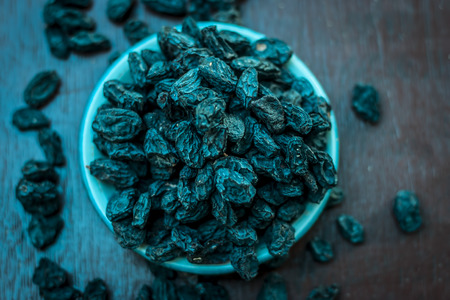 Black raisin or kali kishmish or Zante currant in a white plate on wooden surface in dark Gothic colors to decreases the chance of Dehydration.の写真素材