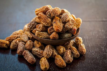 Close up of raw dried dates,Phoenix dactylifera in a traditional bowl on a wooden surface.