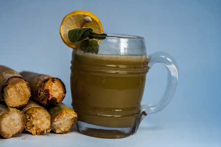 Popular Indian/Asian Ganne ka ras or Sugar cane or Saccharum officinarum juice in a transparent glass with raw sugarcane isolated on white.の写真素材