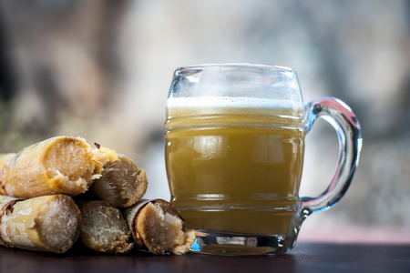 Popular Indian/Asian Ganne ka ras or Sugar cane or Saccharum officinarum juice in a transparent glass with raw sugarcane on a wooden surface in dark Gothic colors with all its ingredients.の写真素材